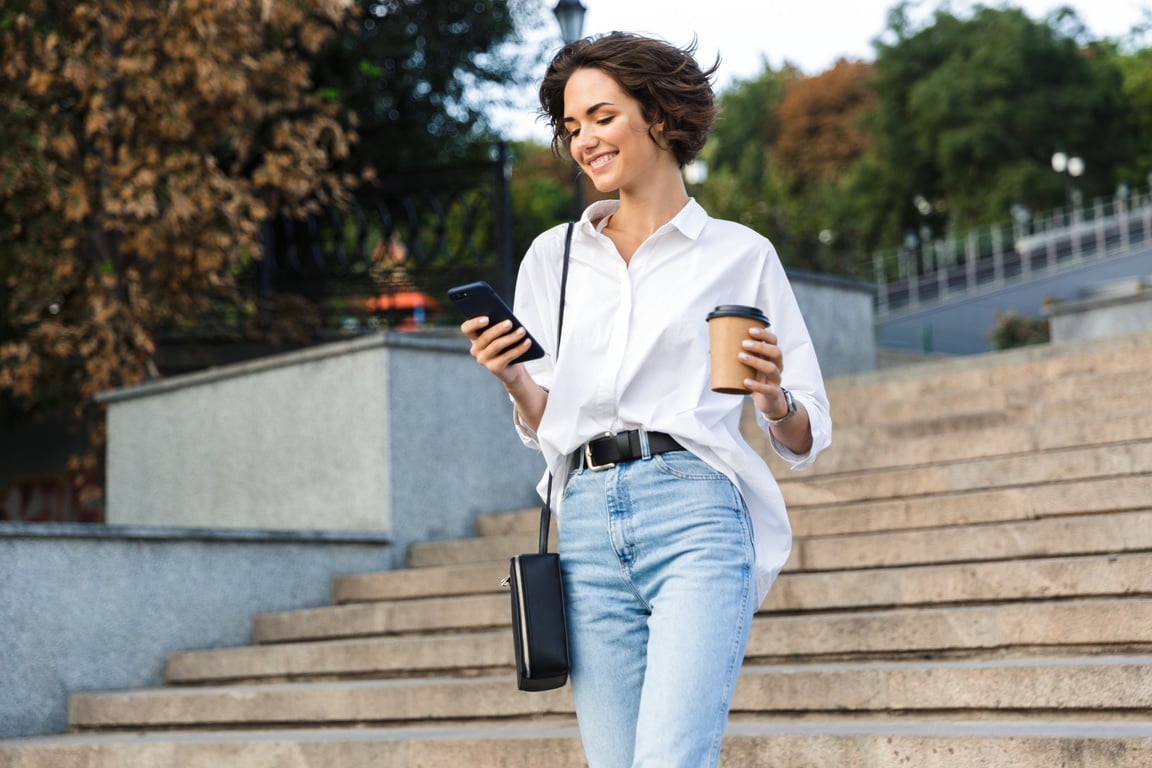 Cute Beautiful Woman Walking on the Street Using Mobile Phone Holding Coffee.